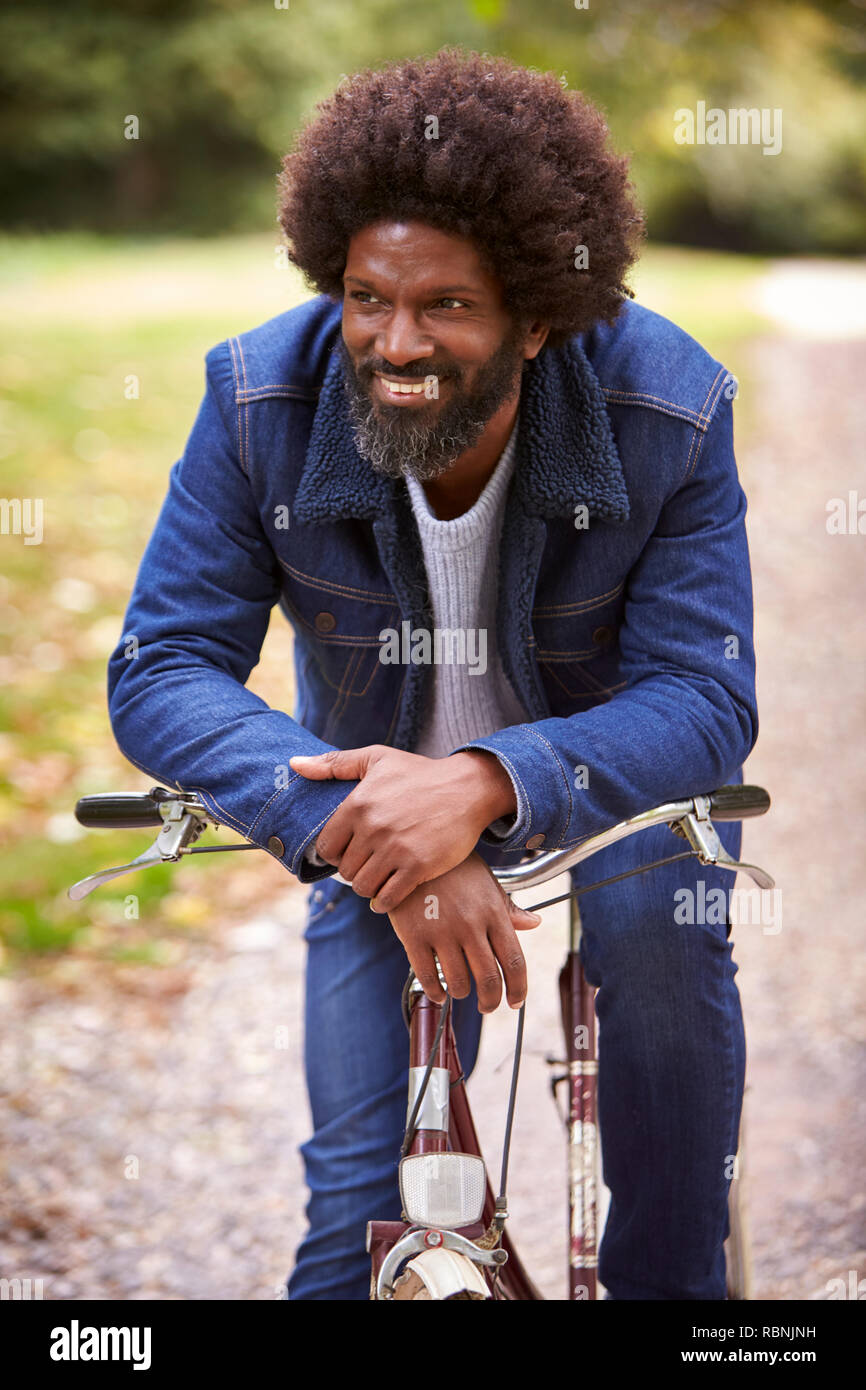 Schwarz im mittleren Alter Mann sitzt auf einem Fahrrad in einem Park, stützte sich auf den Lenker lächelnd, Vorderansicht, in der Nähe Stockfoto