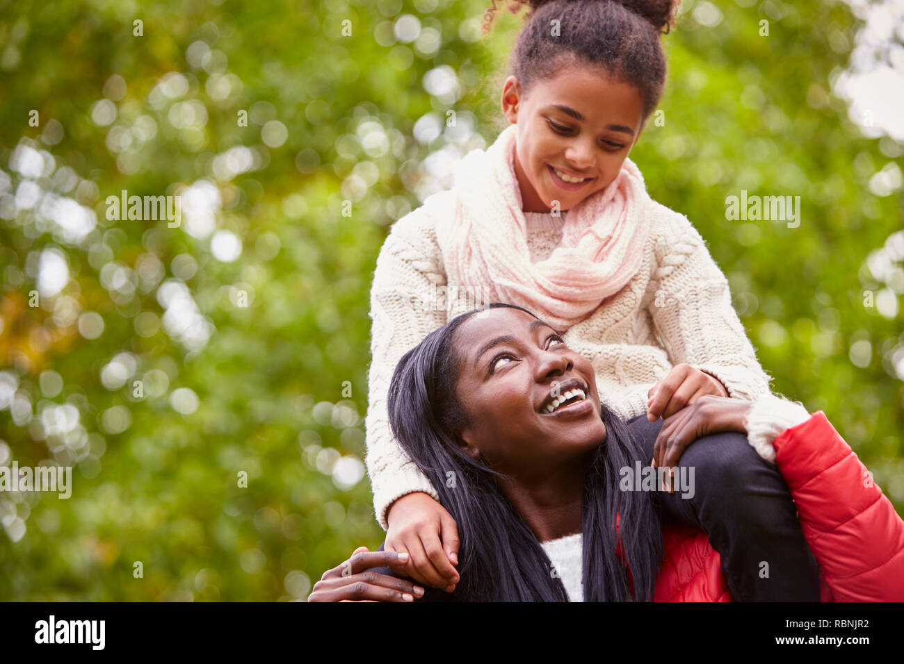 Junge schwarze Frau, die ihr vor - jugendlich Tochter auf ihre Schultern in den Park, die beide ein Lächeln auf jedes andere, in der Nähe Stockfoto