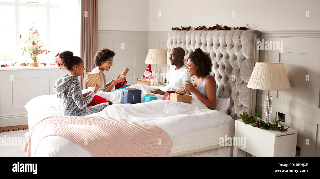 Jungen gemischten Rennen Familie sitzt auf dem Bett öffnen Geschenke im Schlafzimmer der Eltern am Weihnachtsmorgen Stockfoto