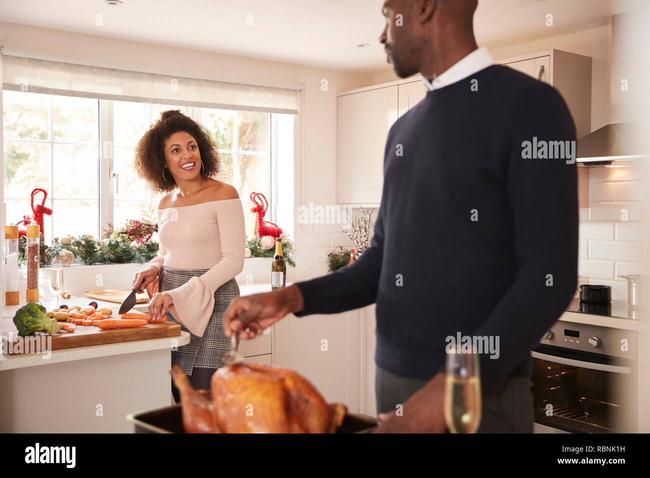 Junge Erwachsene Mixed Race Paar Weihnachtsessen zusammen die Vorbereitung zu Hause, Mann basting Truthahn im Vordergrund sich zu seinem Partner, Frontansicht zu sprechen, in der Nähe Stockfoto