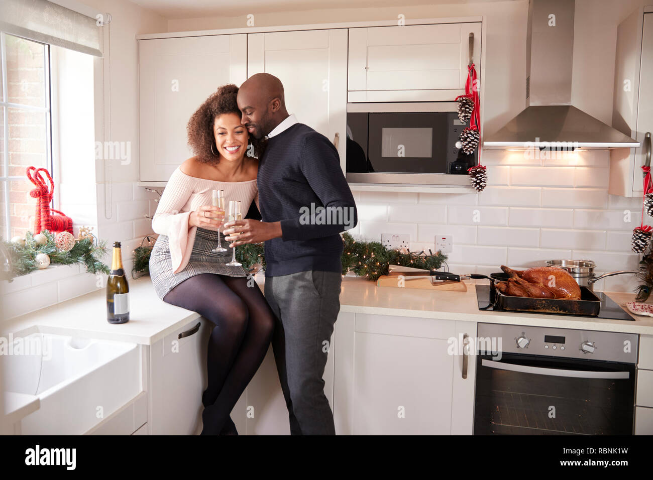 Junge Mixed Race Paar trinken Champagner in Ihrer Küche umarmen, während Weihnachten Abendessen vorbereiten Stockfoto