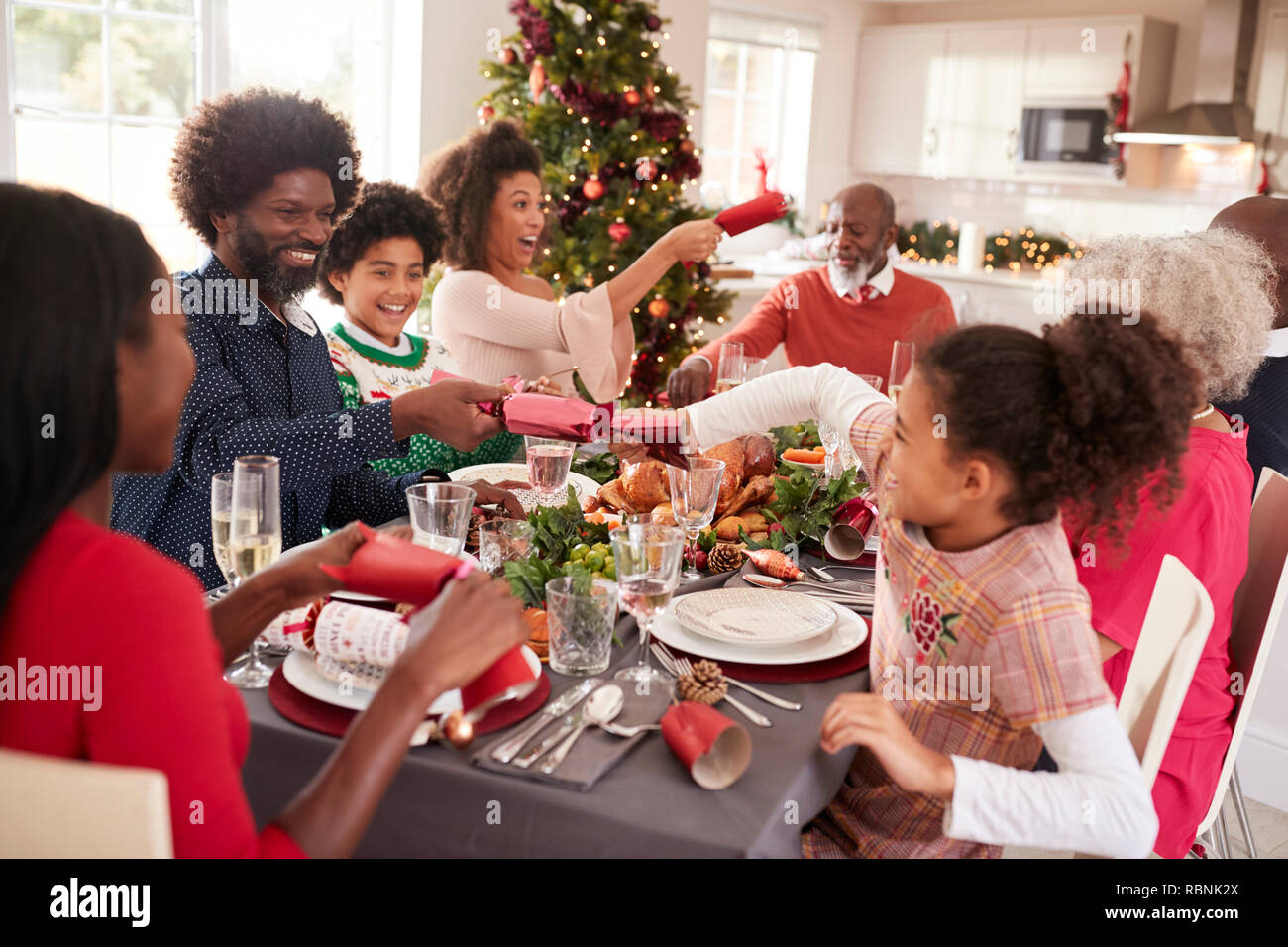Gemischte Rasse, multi-generation Familie Spaß Cracker ziehen am Weihnachtsessen Tabelle Stockfoto