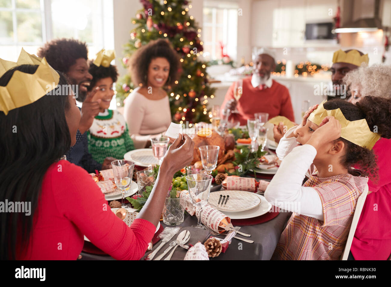Gemischte Rasse, multi-generation Familie das Weihnachtsessen Tabelle Witze lesen sitzen und tragen Papier Partei Hüte von Knallbonbons, Nahaufnahme Stockfoto