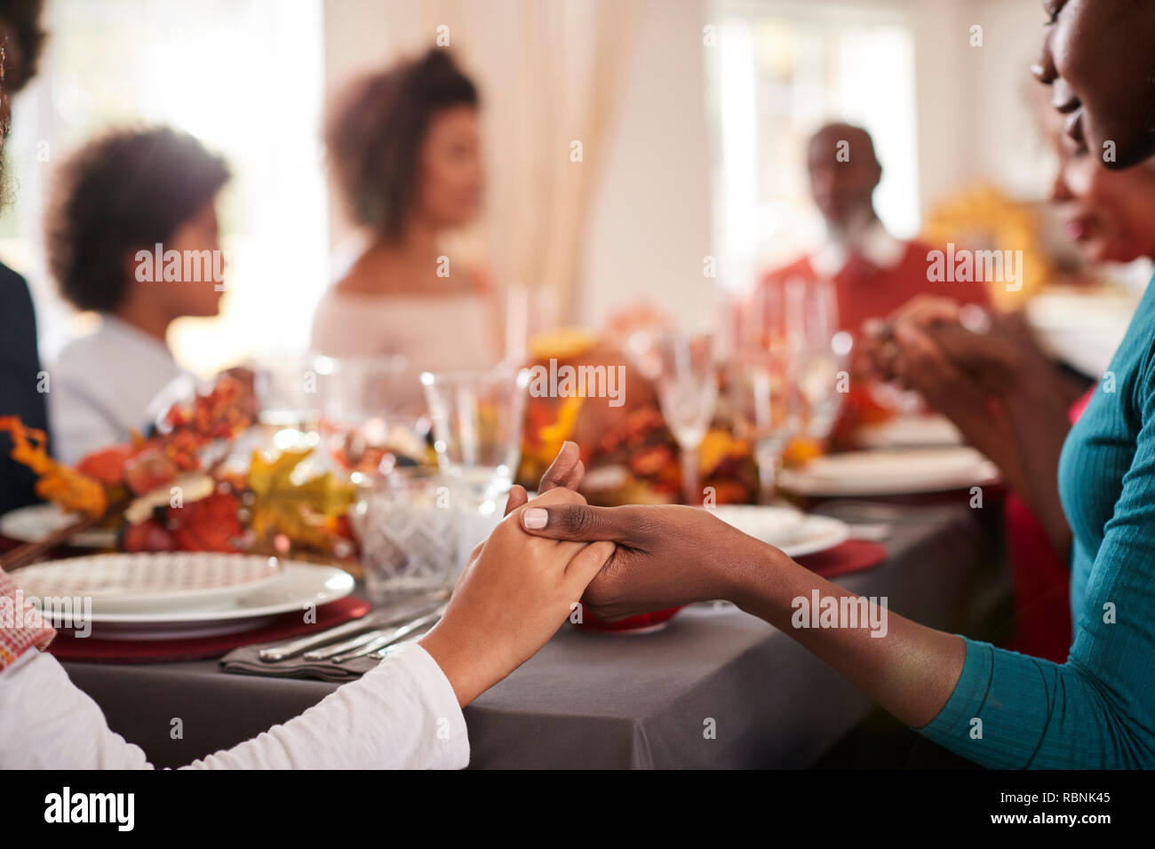 Junge schwarze Frau und Tochter halten sich an den Händen und sagen Gnade mit ihren multi Generation Familie am Thanksgiving Dinner Table, Detail, im Vordergrund Schwerpunkt Stockfoto