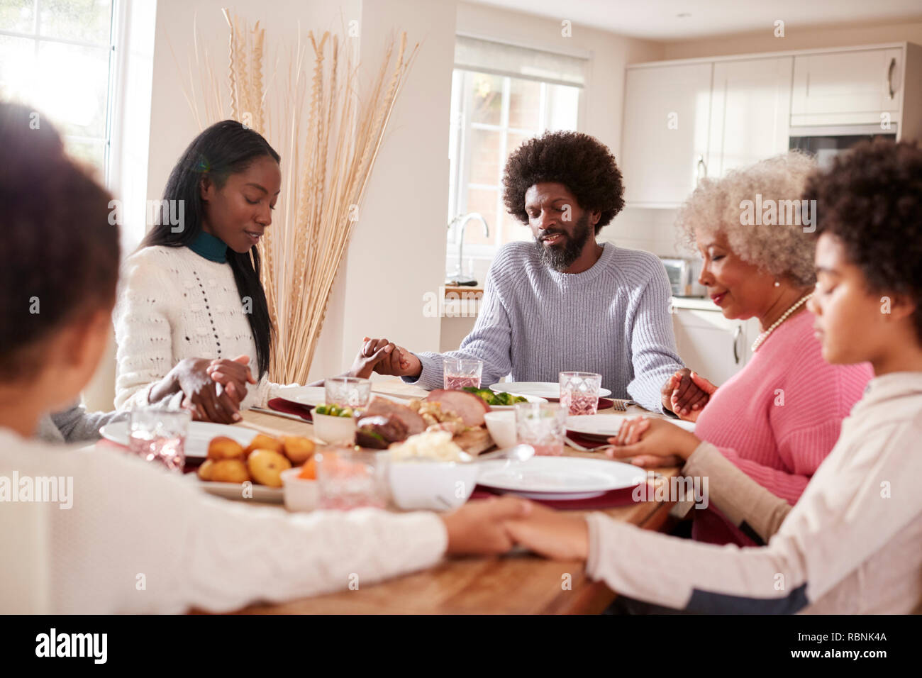 Multi-Generation gemischten Rennen Familie halten sich an den Händen und sagen Gnade vor dem Essen ihren Sonntag Abendessen Stockfoto
