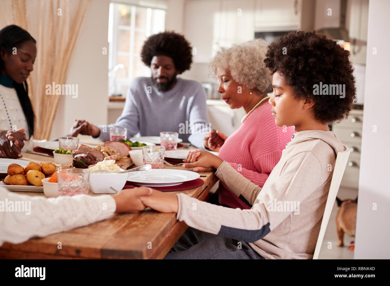 Multi-Generation gemischten Rennen Familie halten sich an den Händen und sagen Gnade vor dem Essen ihren Sonntag Abendessen, Seitenansicht Stockfoto