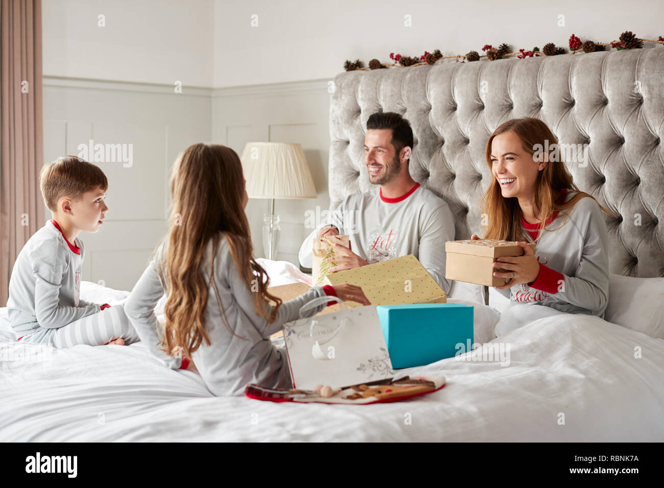 Aufgeregte Kinder sitzen am Bett der Eltern zu Hause, Familie Geschenke an Weihnachten Stockfoto