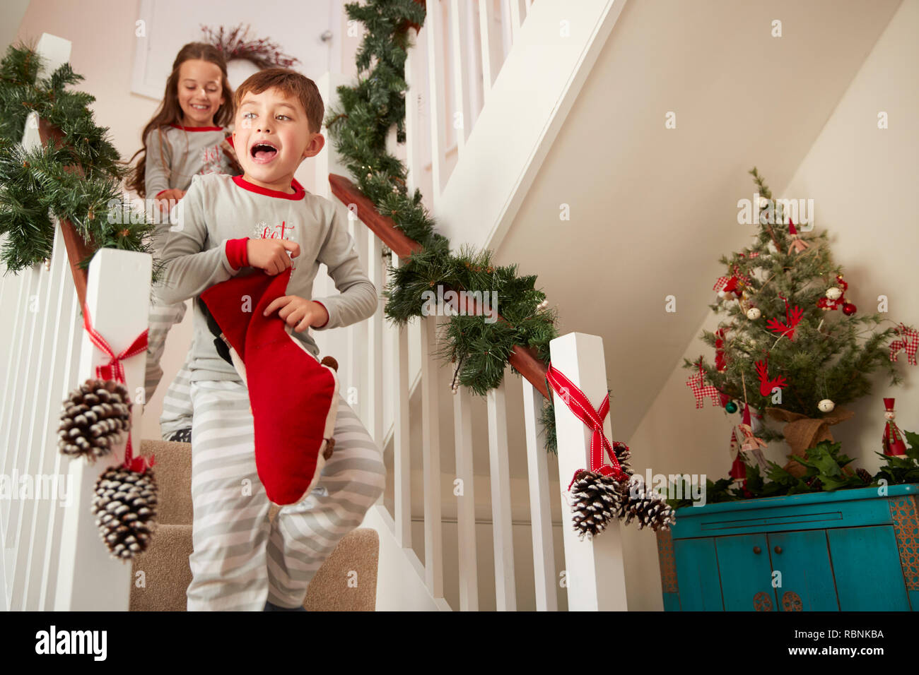 Zwei aufgeregte Kinder Schlafanzüge tragen, läuft die Treppe hinunter Holding Strümpfe am Weihnachtsmorgen Stockfoto