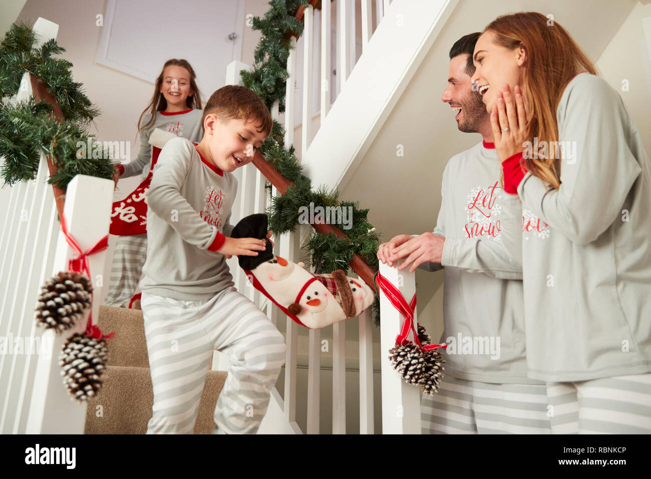 Eltern Gruß aufgeregte Kinder Schlafanzüge tragen, läuft die Treppe hinunter Holding Strümpfe am Weihnachtsmorgen Stockfoto