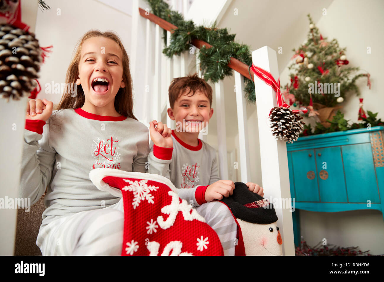 Porträt von zwei aufgeregte Kinder Schlafanzüge tragen, Sitzen auf der Treppe Holding Strümpfe am Weihnachtsmorgen Stockfoto