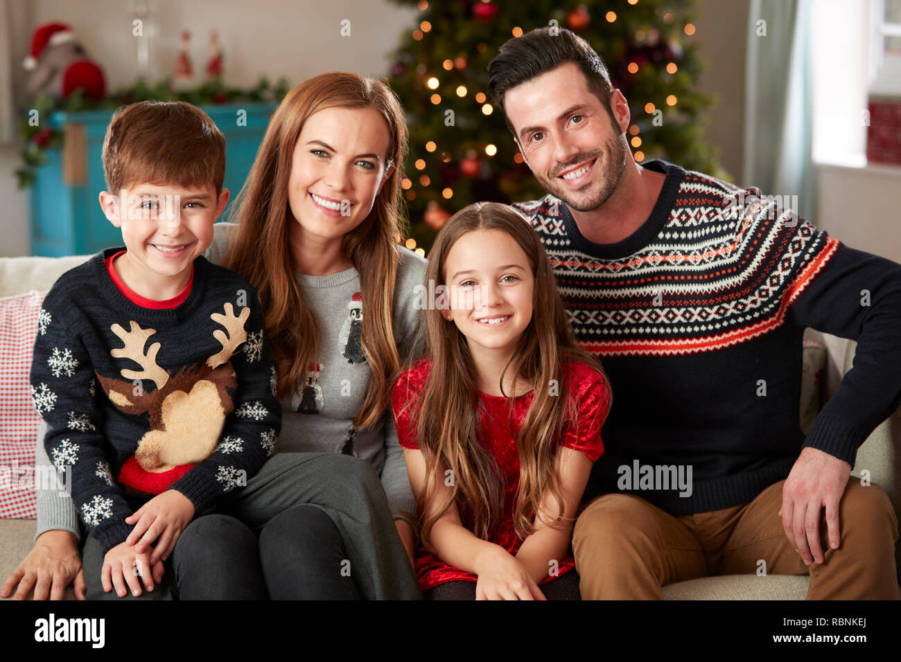 Portrait von Eltern mit Kindern tragen Festliche Jumper sitzt auf einem Sofa im Wohnzimmer zu Hause an Weihnachten Stockfoto
