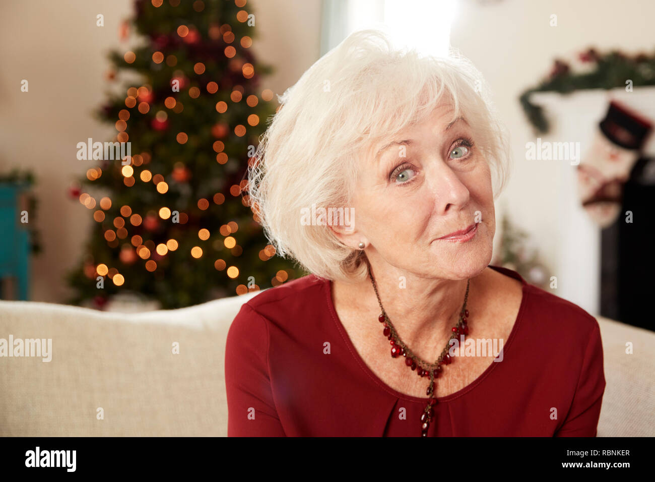 Portrait der älteren Frau sitzt auf einem Sofa im Wohnzimmer zu Hause an Weihnachten