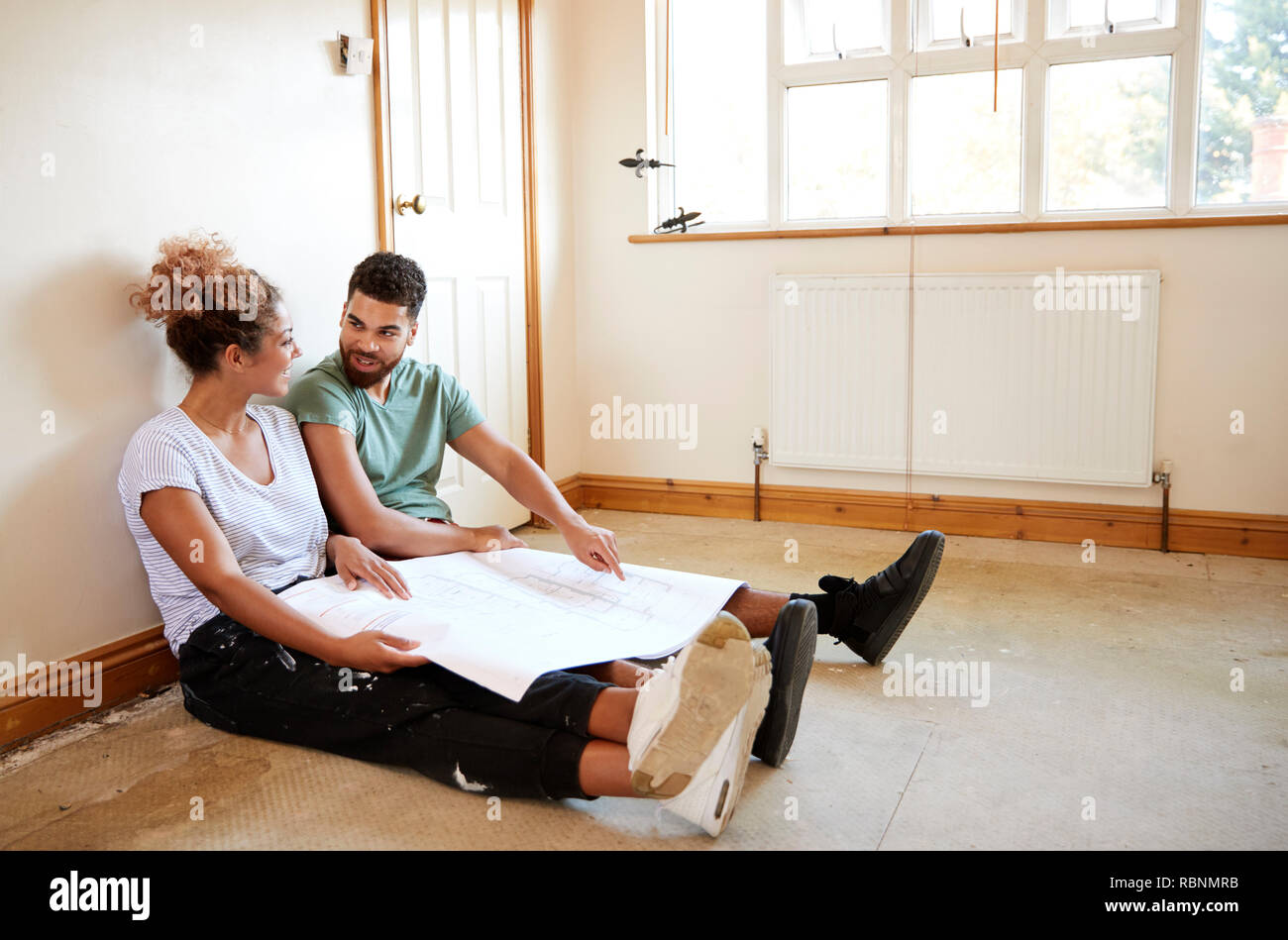 Paar sitzen auf dem Boden an Pläne im leeren Raum der neuen Home Suchen Stockfoto
