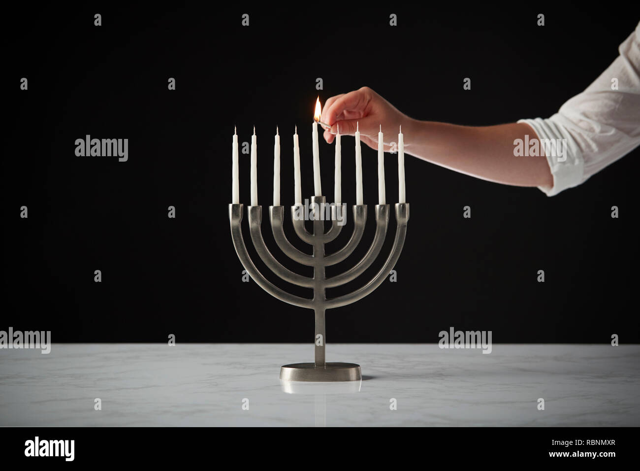Beleuchtung Kerze auf Metall Hanukkah Menorah auf Marmor Oberfläche gegen Schwarz Studio Hintergrund Stockfoto