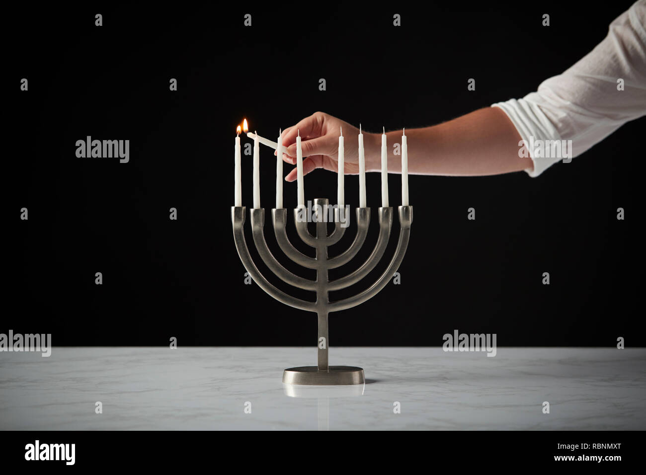 Beleuchtung Kerze auf Metall Hanukkah Menorah auf Marmor Oberfläche gegen Schwarz Studio Hintergrund Stockfoto