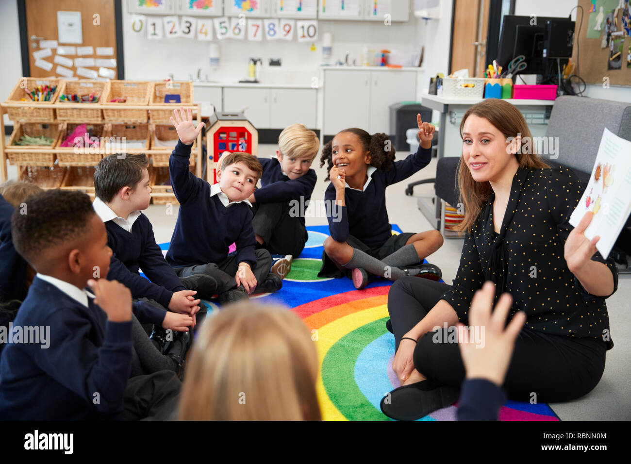 Grundschule Kinder sitzen auf dem Boden in einem Klassenzimmer mit ihrer Lehrerin, die Hände eine Frage, selektiven Fokus auf Antwort Stockfoto