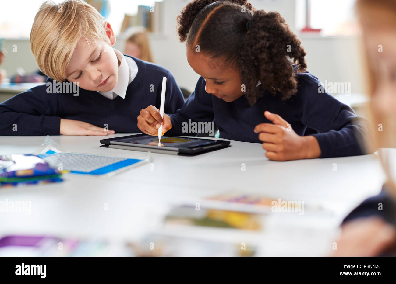 Schülerin mit einem Tablett und Stift mit einem Jungen sitzen an einem Tisch in einer Grundschule Klassenzimmer, selektiven Fokus Stockfoto