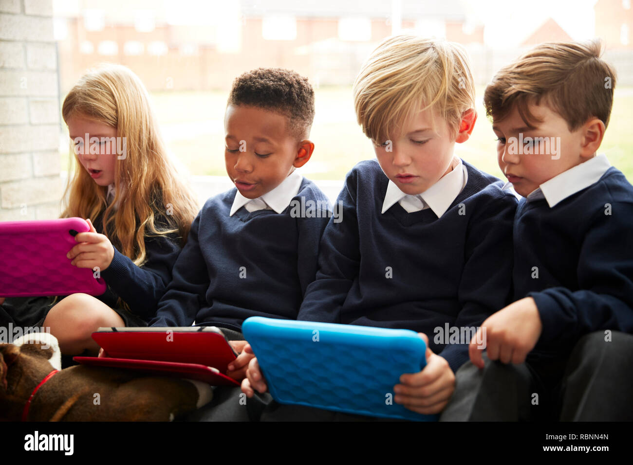 Vier der Grundschule, Kinder sitzen auf dem Boden vor einem Fenster mit Tablet-pcs während der Pause Zeit, in der Nähe Stockfoto