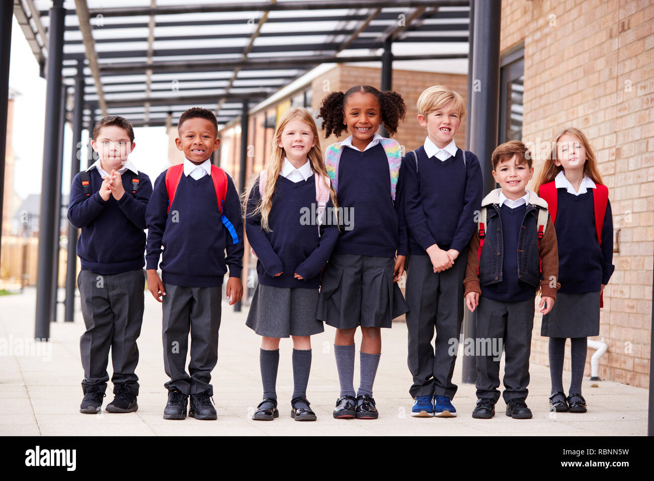 Grundschule Kinder stehen in einer Reihe auf einem Gehweg außerhalb ihrer Schule, lächelnd auf Kamera, niedrigen Winkel Stockfoto