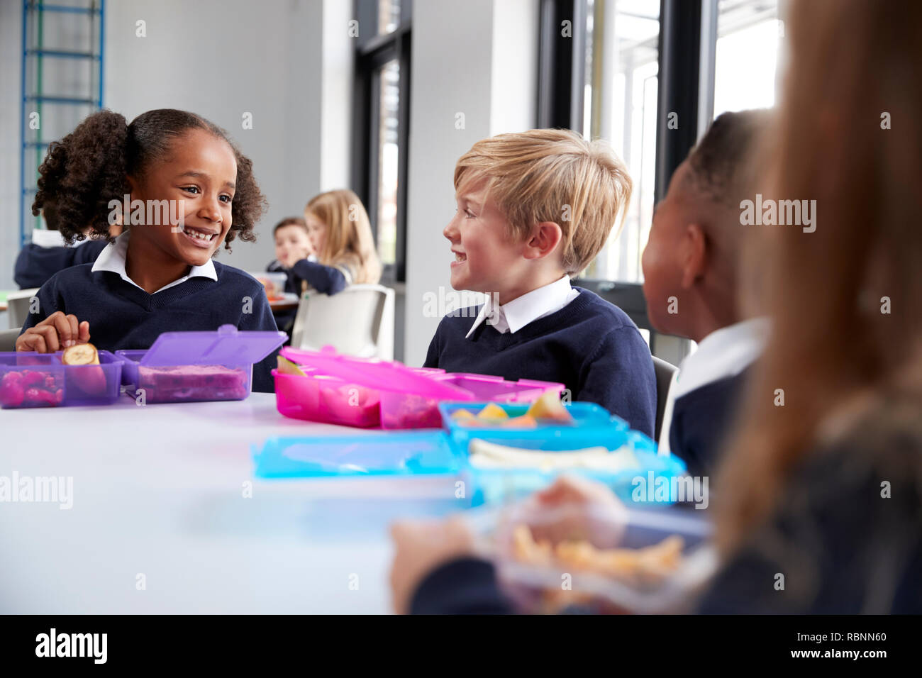 Grundschule Kinder sitzen am Tisch essen ihre Lunchpakete und sprechen, in der Nähe Stockfoto
