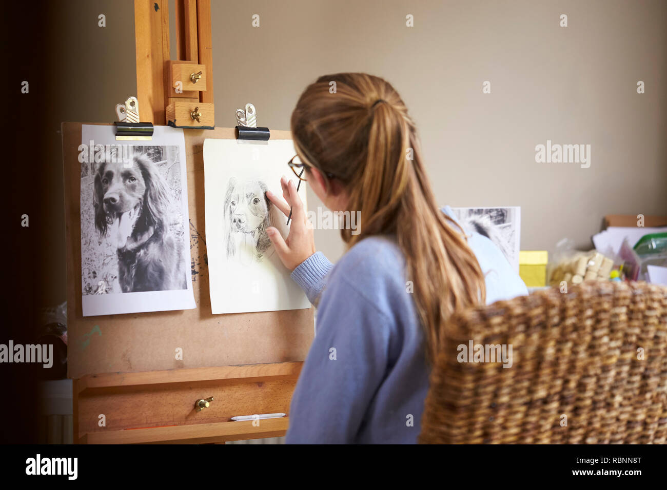 Ansicht der Rückseite des weiblichen Teenager Künstler sitzen an Staffelei Zeichnung Bild von Hund von Foto in Anthrazit Stockfoto