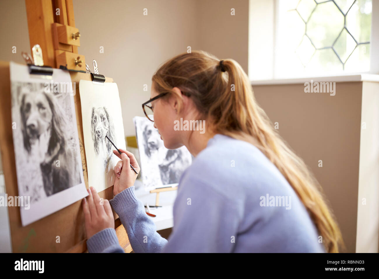 Seitenansicht der weiblichen Teenager Künstler sitzen an Staffelei Zeichnung Bild von Hund von Foto in Anthrazit Stockfoto