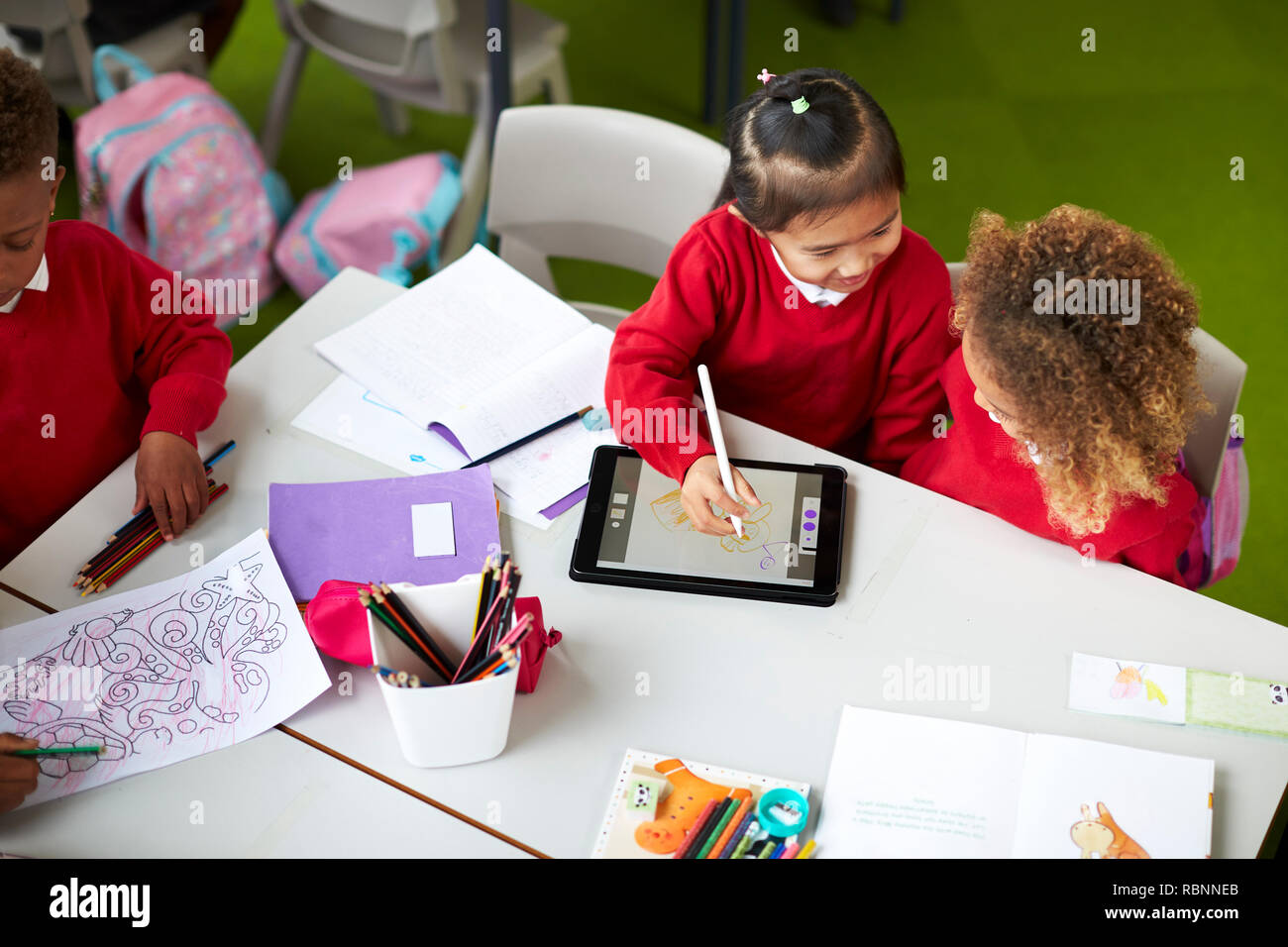 Aussicht auf zwei Infant school Mädchen an einem Tisch sitzen erhöht, mit einem Tablet Computer und Stylus in einem Klassenzimmer Stockfoto