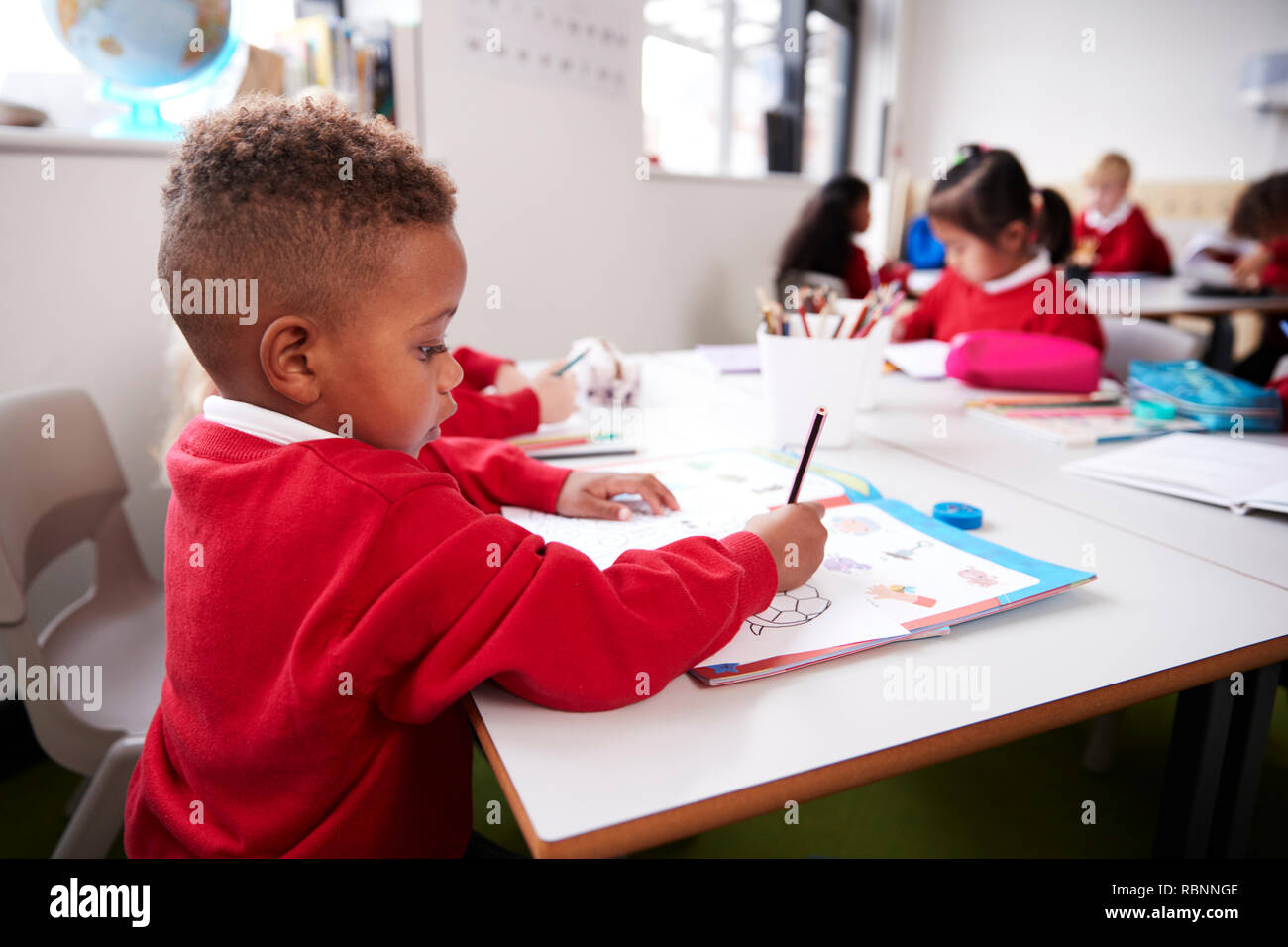 Junge schwarze Schüler tragen Schuluniform an einem Schreibtisch in einem Kind Schule Klassenzimmer Zeichnung sitzend, Nahaufnahme, Seitenansicht Stockfoto
