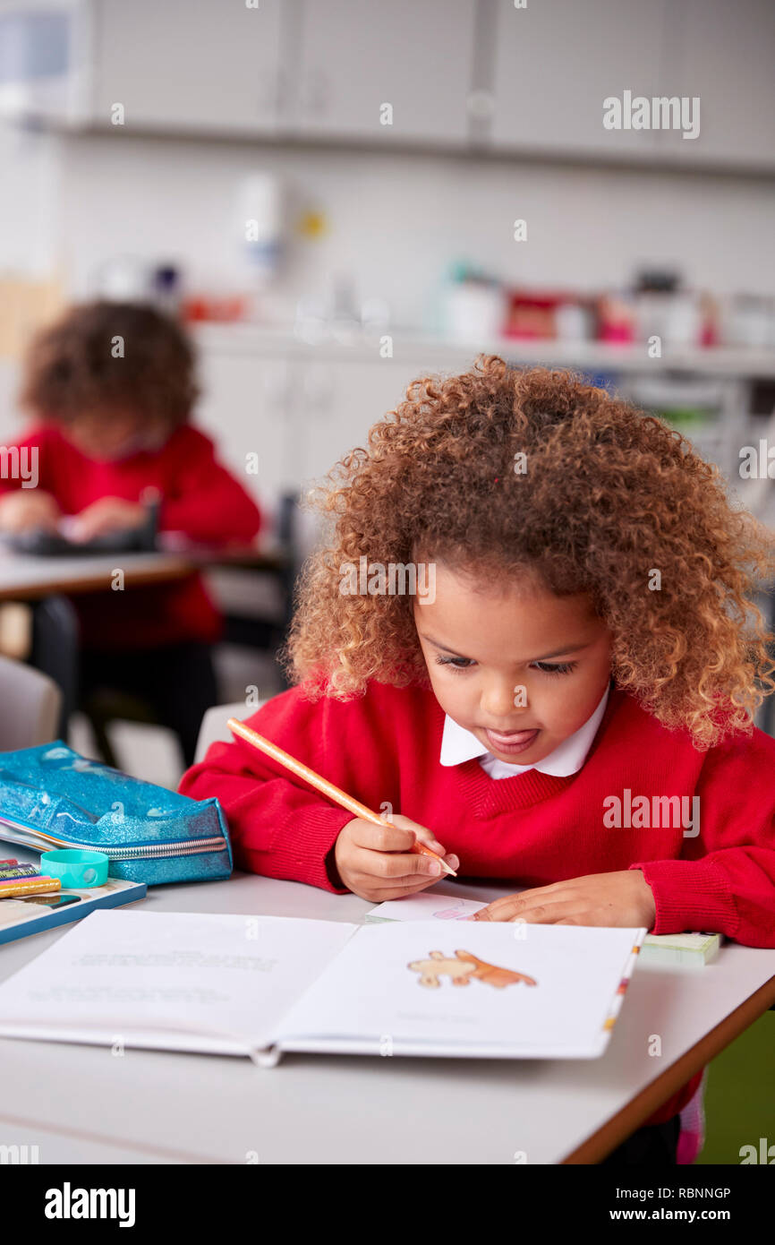 Nahaufnahme von gemischten Rennen Schülerin an Schreibtisch in einem Kind Schule Klassenzimmer Zeichnung sitzen, vertikal Stockfoto