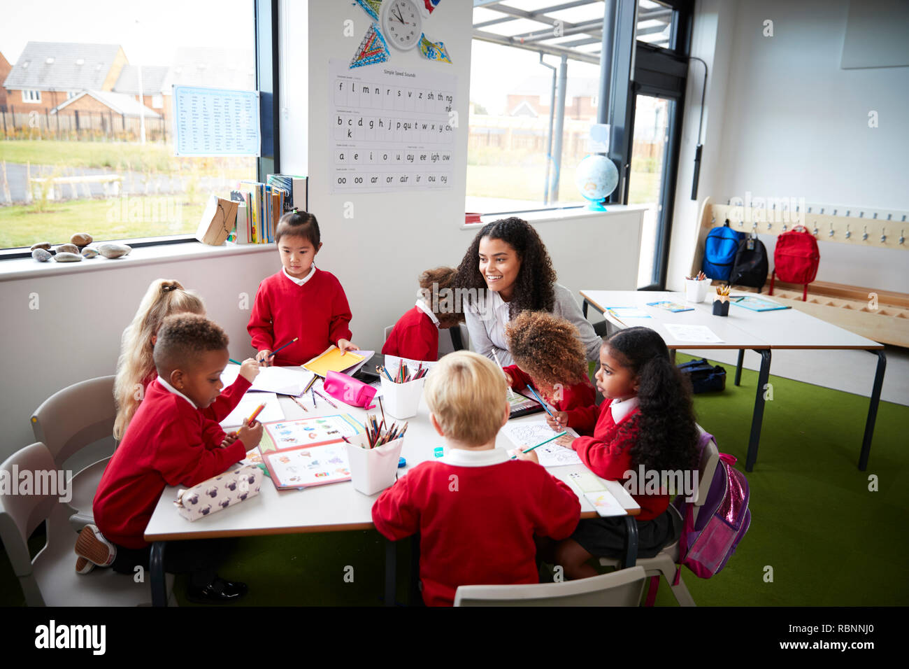 Eine Gruppe von Infant School Kids an einem Tisch in einem Klassenzimmer sitzen mit ihrer Lehrerin Stockfoto