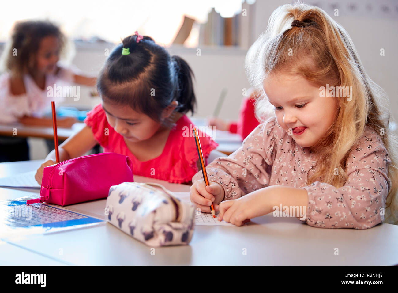 Zwei junge Schülerinnen an einem Schreibtisch in einem Kind Schule Klassenzimmer sitzend arbeiten, in der Nähe Stockfoto