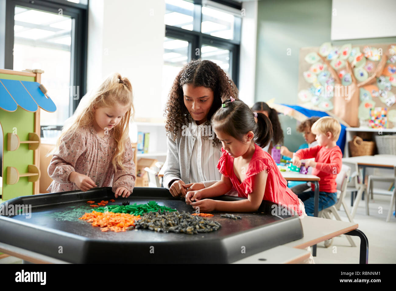 Zwei junge Schülerinnen stehend an einem Tisch spielen ein Spiel mit Ihrer Lehrerin in einem Kind Schule Klassenzimmer, selektiven Fokus Stockfoto