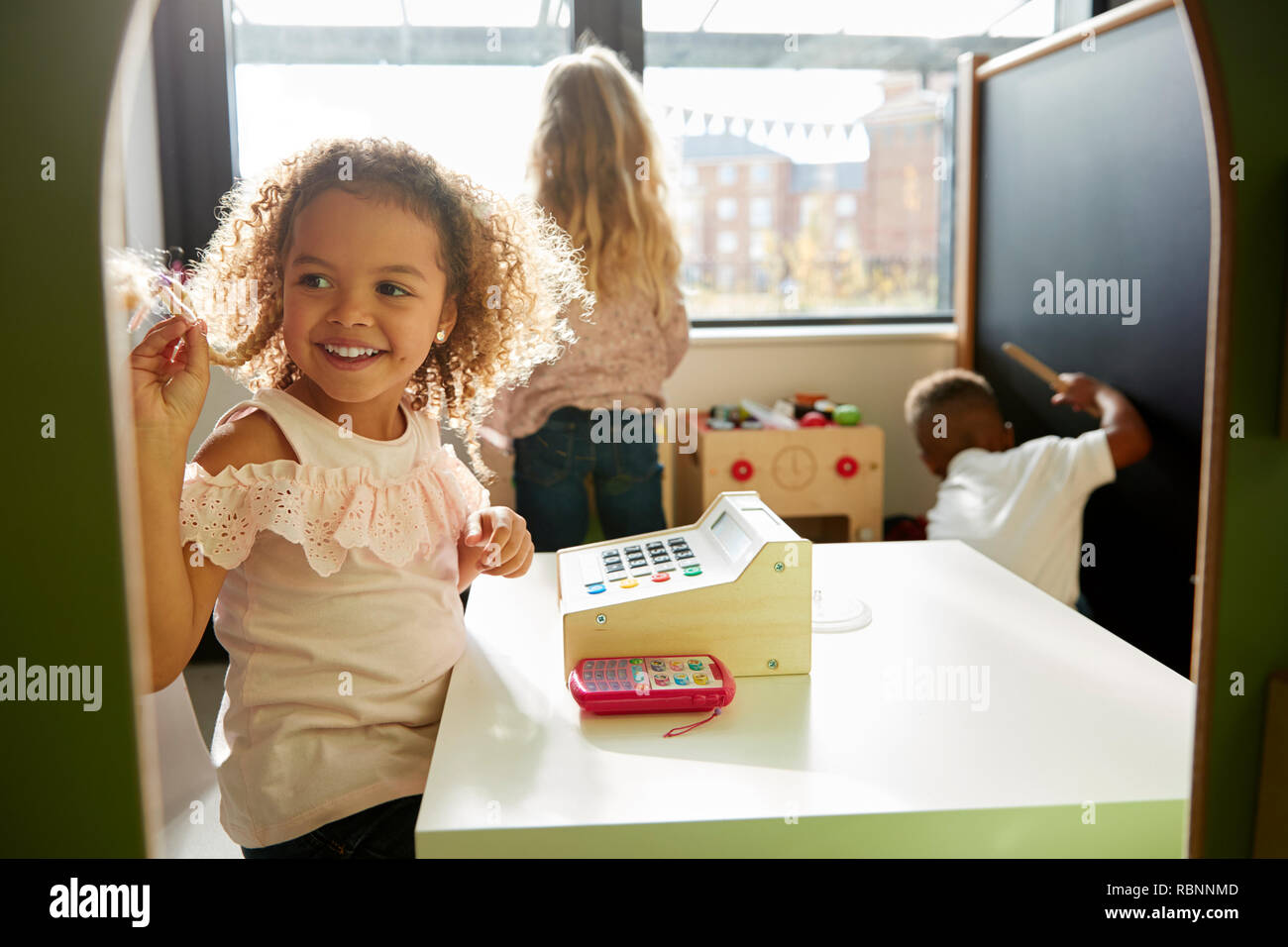 Zwei junge Mädchen und ein Junge, die zusammen spielen in einem Spielhaus an Infant School, Hintergrundbeleuchtung Stockfoto