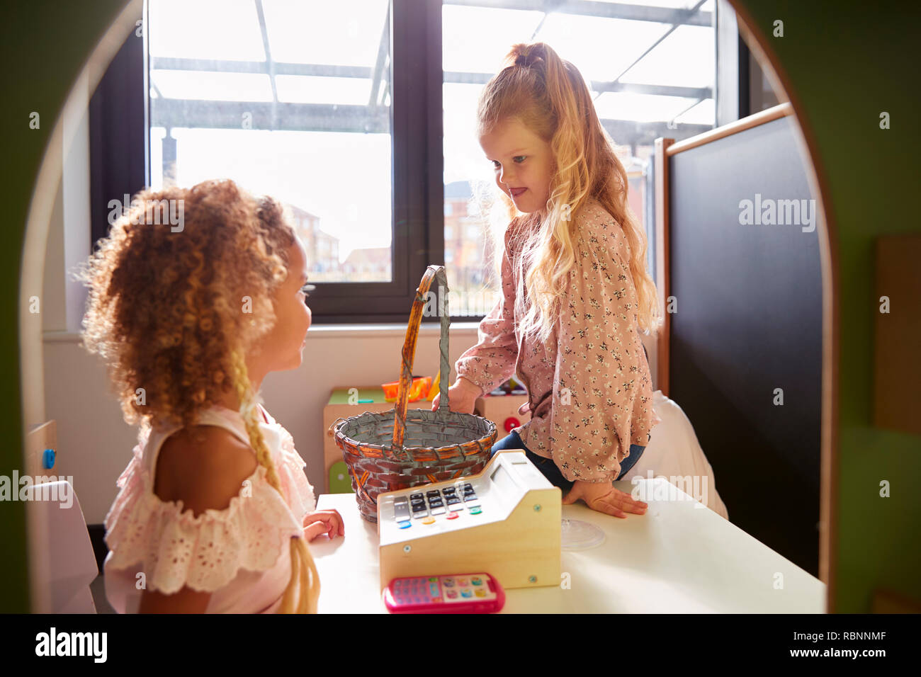 Zwei junge Schülerinnen spielen Shop in einem Spielhaus bei einem Kleinkind Schule, Hintergrundbeleuchtung Stockfoto