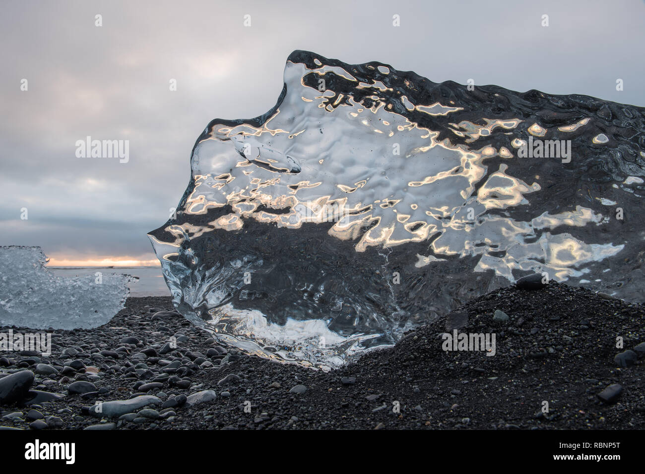Sun Reflexion in transparenten Eisberg auf steinigem Strand Stockfoto