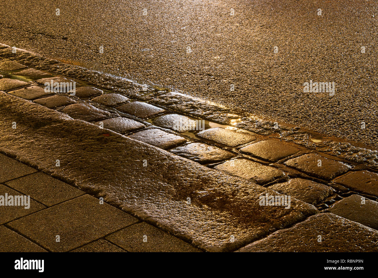 Golden beleuchtete Rinne auf nasser Straße Stockfoto