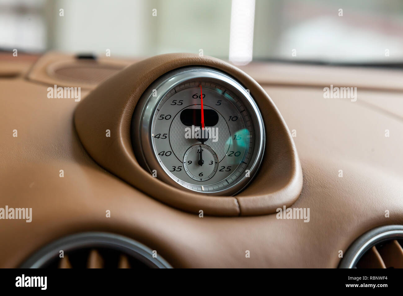 Die Uhr auf dem Armaturenbrett eines teuren Auto ist Close-up, mit  natürlichen Beige Leder überzogen, mit weißem Zifferblatt, ein roter Pfeil  und ein Metall chrom Felge Stockfotografie - Alamy