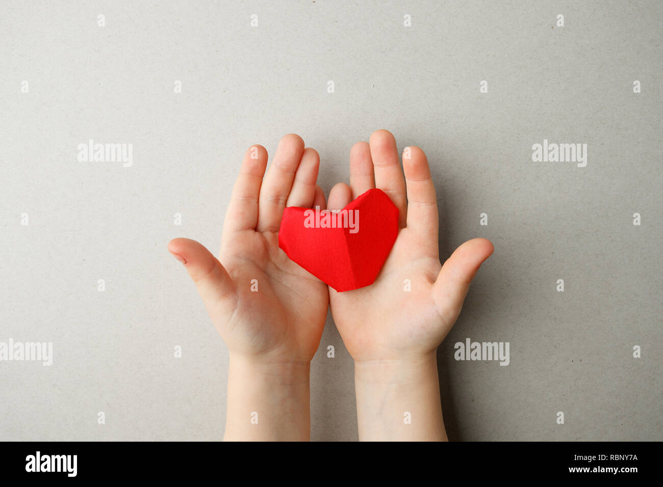 Erwachsene und Kinder Hände halten roten origami Papier Herz in Händen auf grauem Hintergrund Kopie Raum, flach. Valentinstag, Muttertag Liebe und Gesundheit c Stockfoto