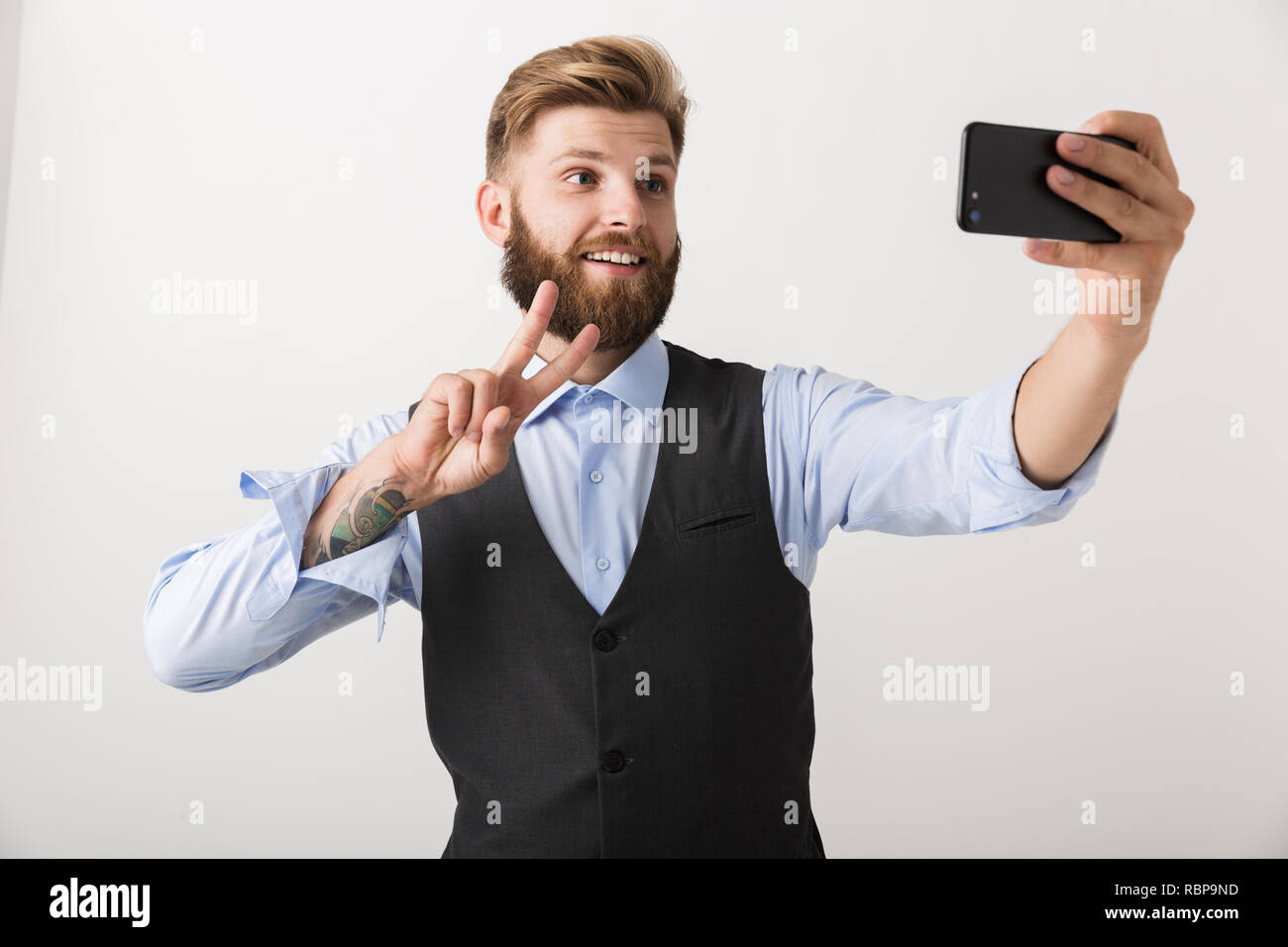 Bild von ein hübscher junger bärtiger Mann stehend über weiße Wand Hintergrund nehmen ein selfie per Handy. Stockfoto