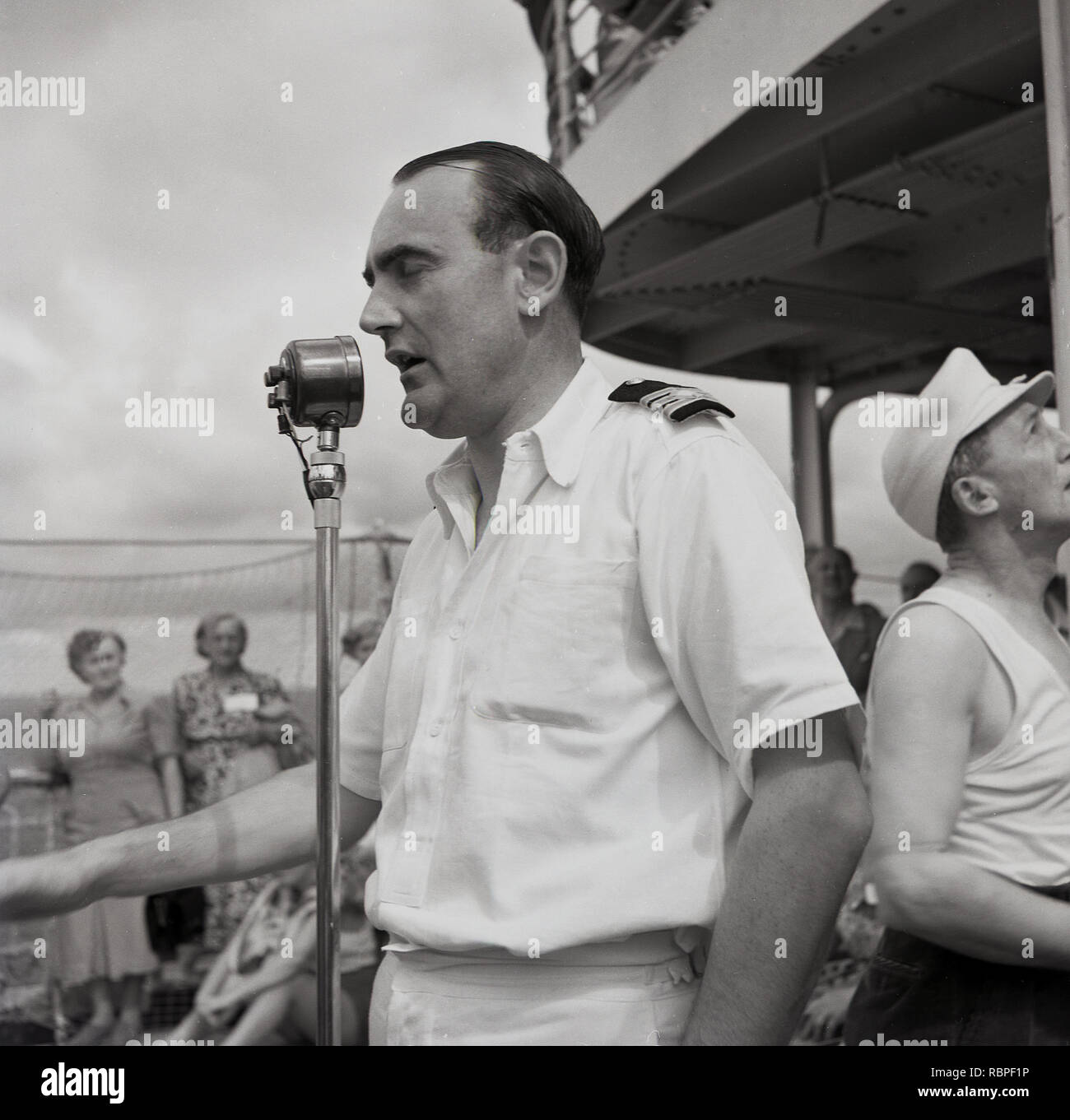 1950, historische, eine männliche Offizier auf dem Deck auf eine Union - Schloss steamship ständigen Durchsage an eine Passagiere am Mikrofon, Stockfoto