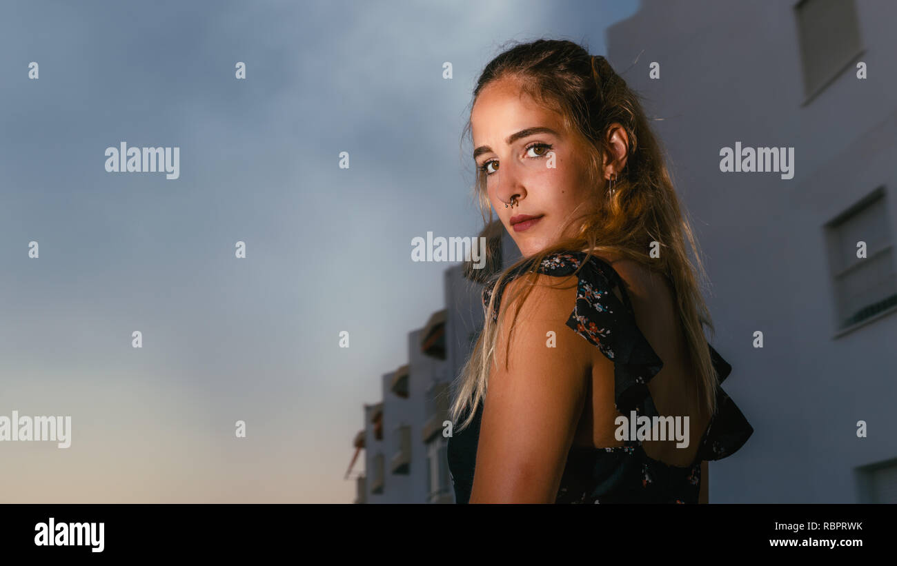 Party-bekleideten Mädchen auf der Straße sieht auf Kamera, im Sommer den Sonnenuntergang. Low Angle Shot von einem schönen Mädchen mit Piercings, lange blonde Haare und Stockfoto