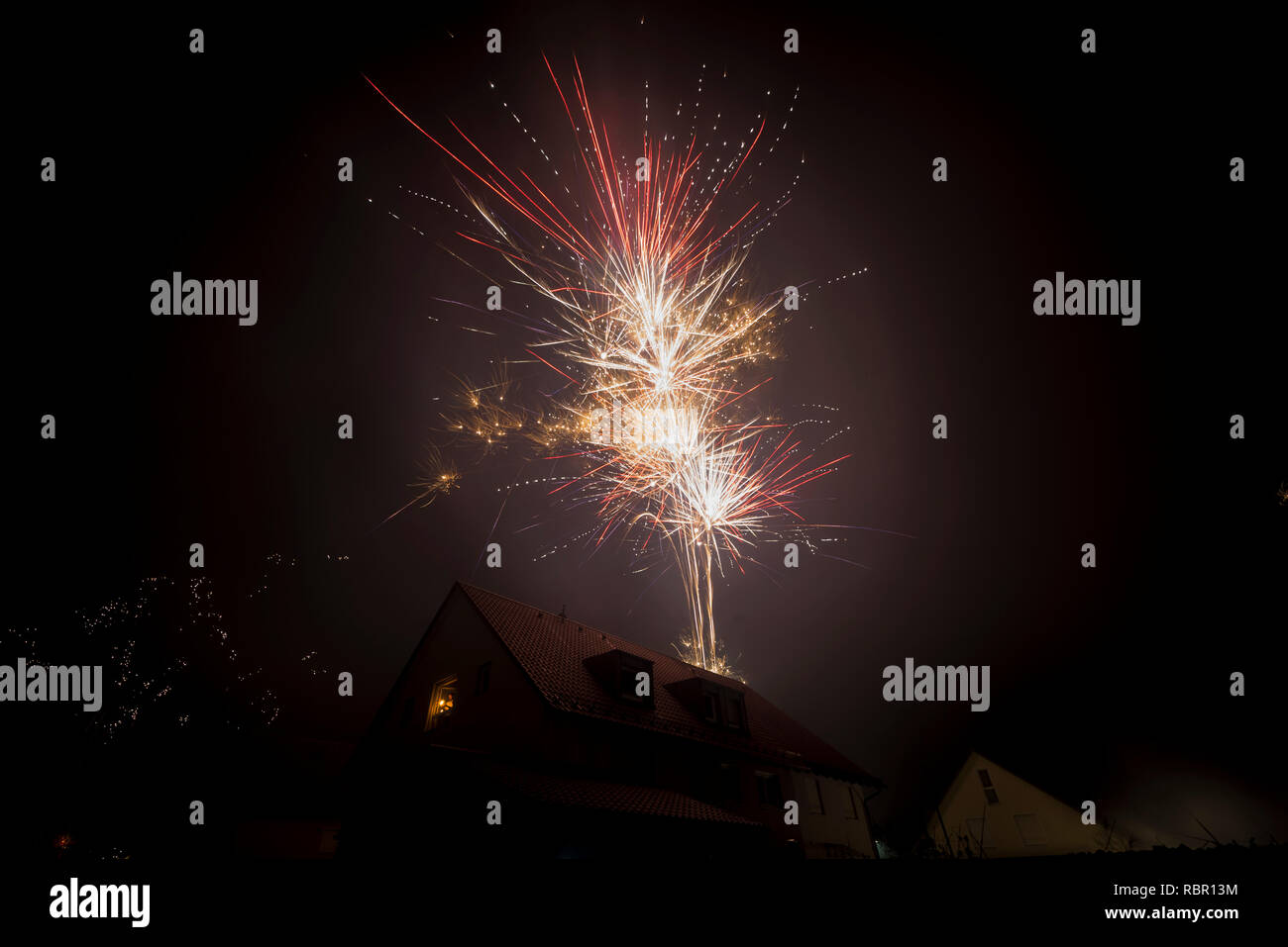 Mann mit Wunderkerzen im Fenster eines Wohnhauses wir das Feuerwerk Aufhellung des Nachthimmels zu Neujahr Stockfoto