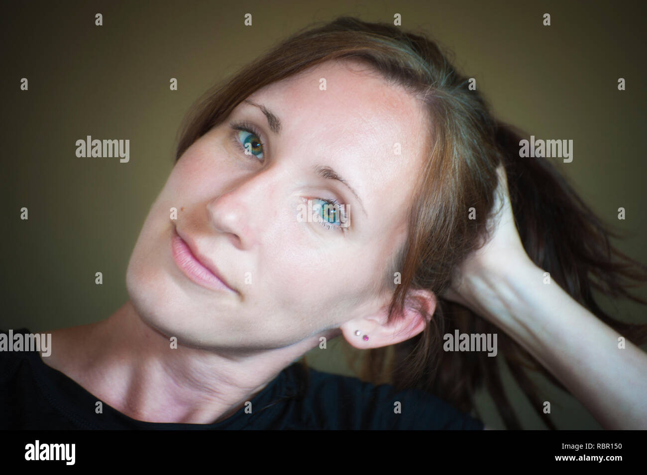 Eine junge Frau ihren Kopf seitlich geneigt ruht in der Hand. Ihre langen Haare in einem Pferdeschwanz ihr Sommersprossige blau grüne Augen in die Kamera Stockfoto