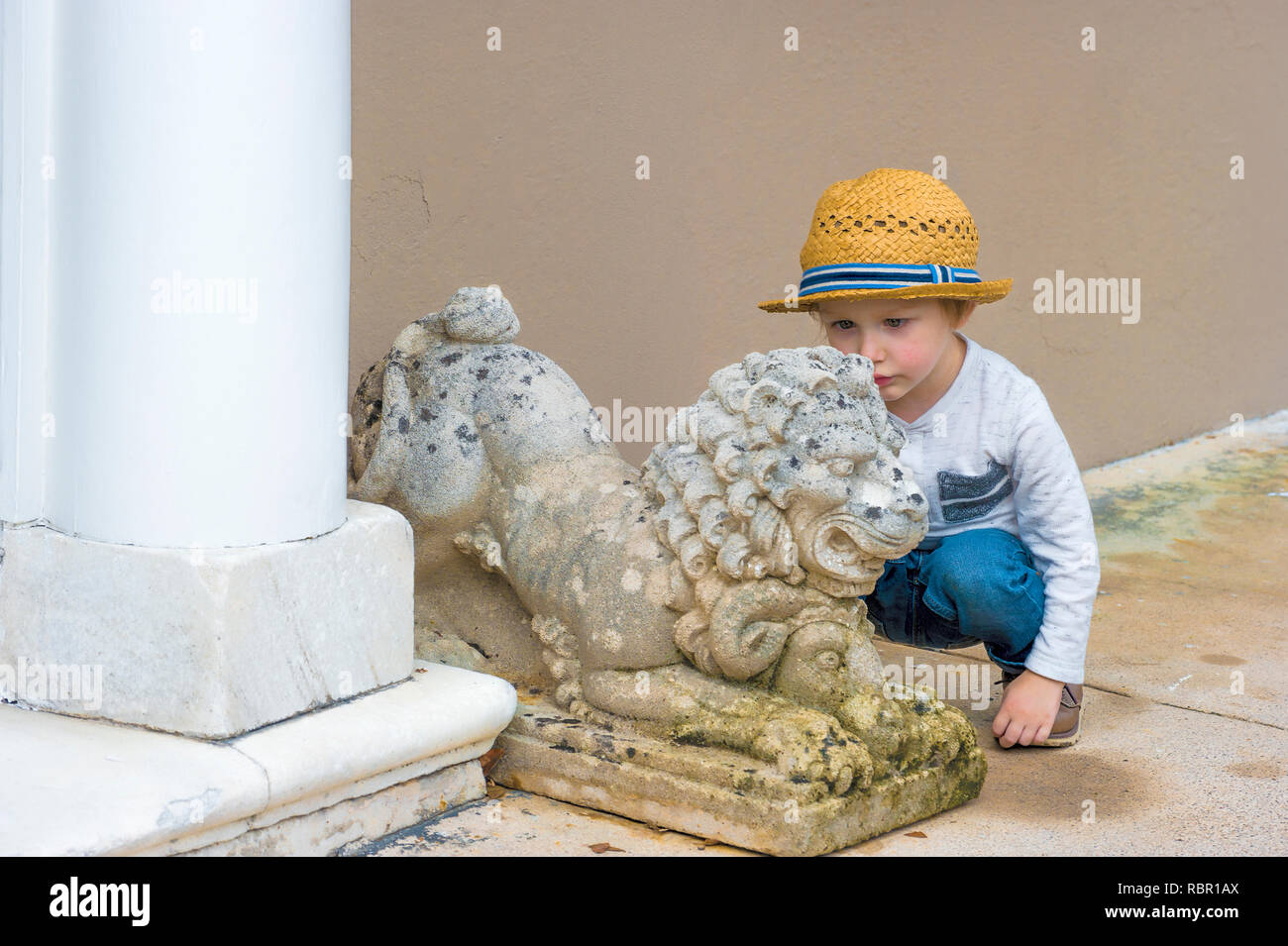 Ein kleiner Junge Kontrollen einen Outdoor rasen Schmuck der Zement lion Satzung. Stockfoto