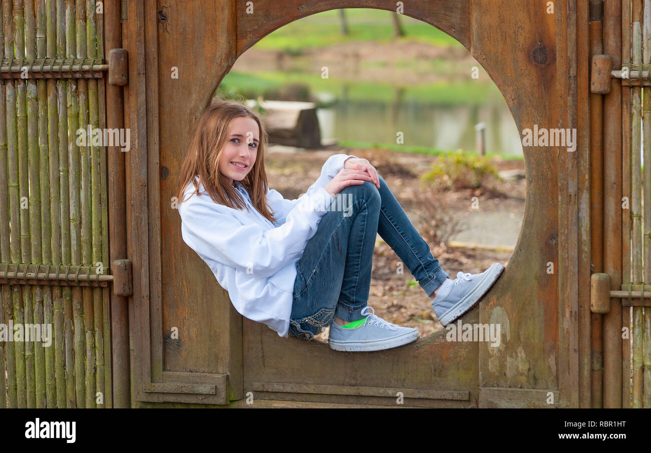 Posieren für die Kamera ein junges Mädchen mit einem weißen Pulli und Jeans in einem Bambus Rahmen in einem öffentlichen Park befindet. Stockfoto