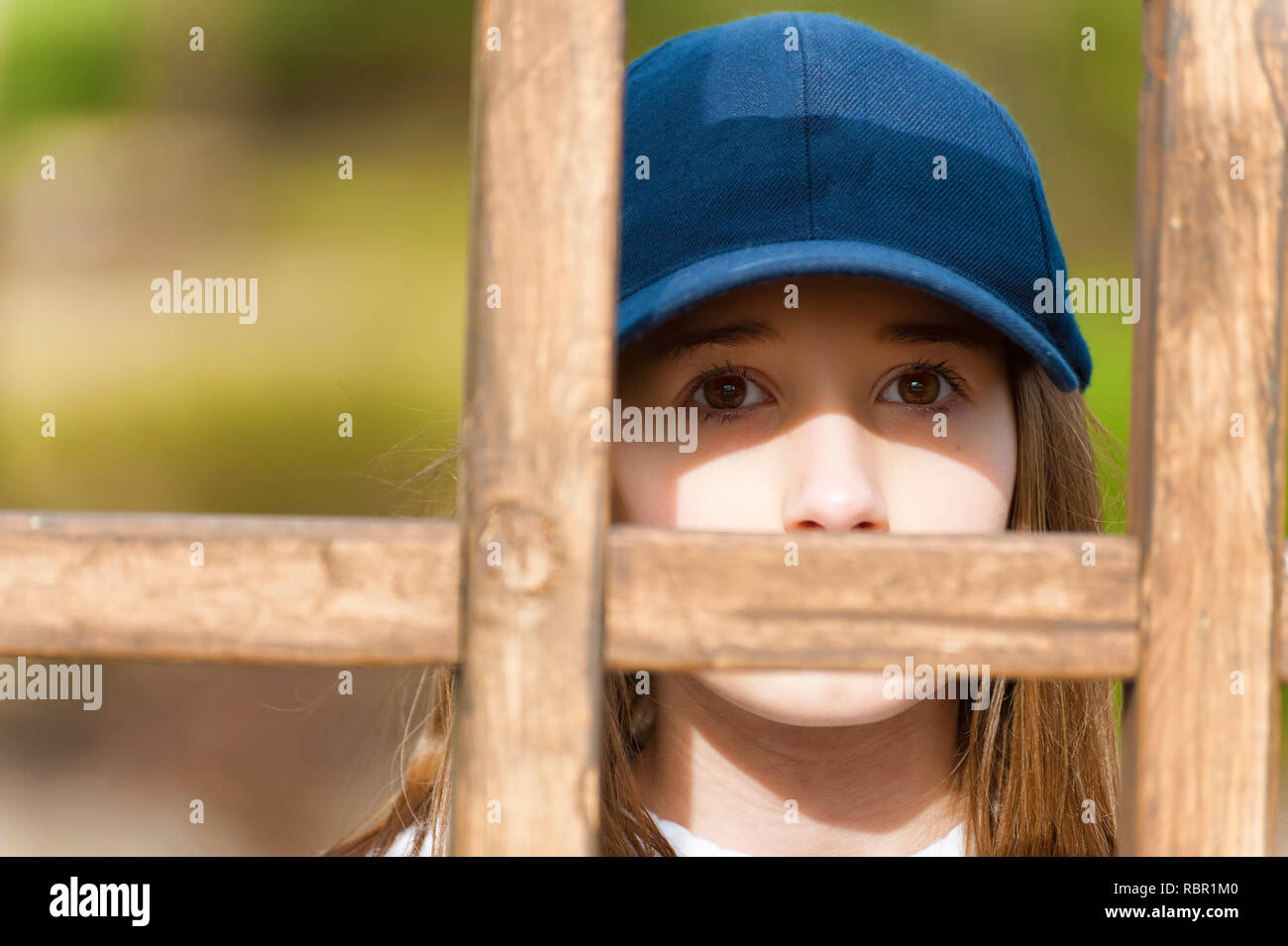 Nahaufnahme eines jungen Mädchens peering von behine Eine hölzerne latice trägt einen blauen Ball Cap Stockfoto