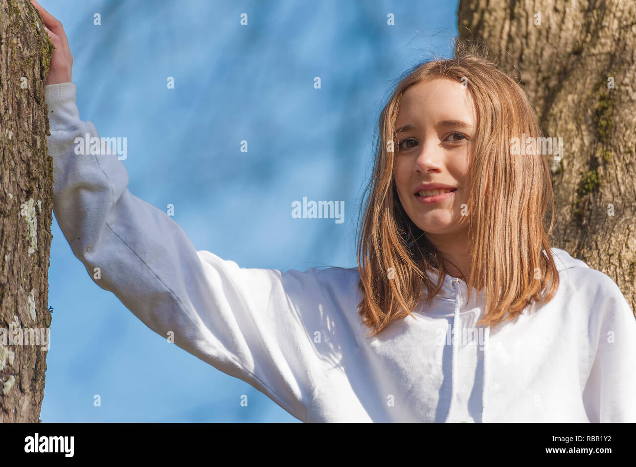 Nahaufnahme von einem jungen Mädchen, das in einem Baum mit braunen Haaren lächelnd und mit Blick auf die Kamera Stockfoto