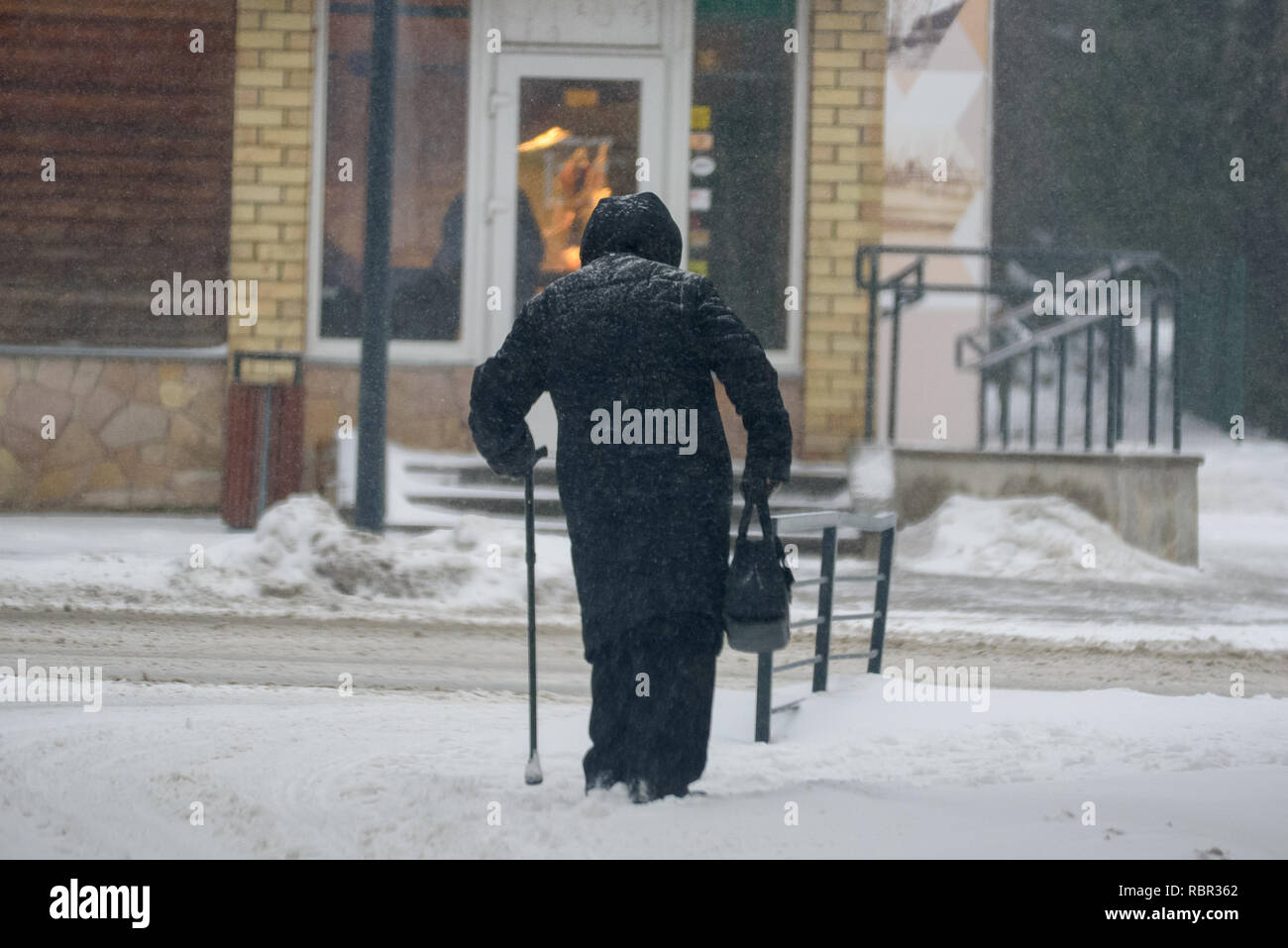 11.01.2019. SALASPILS, Lettland. Eine alte Dame mit Stock wandern, bei Schneefall. Stockfoto