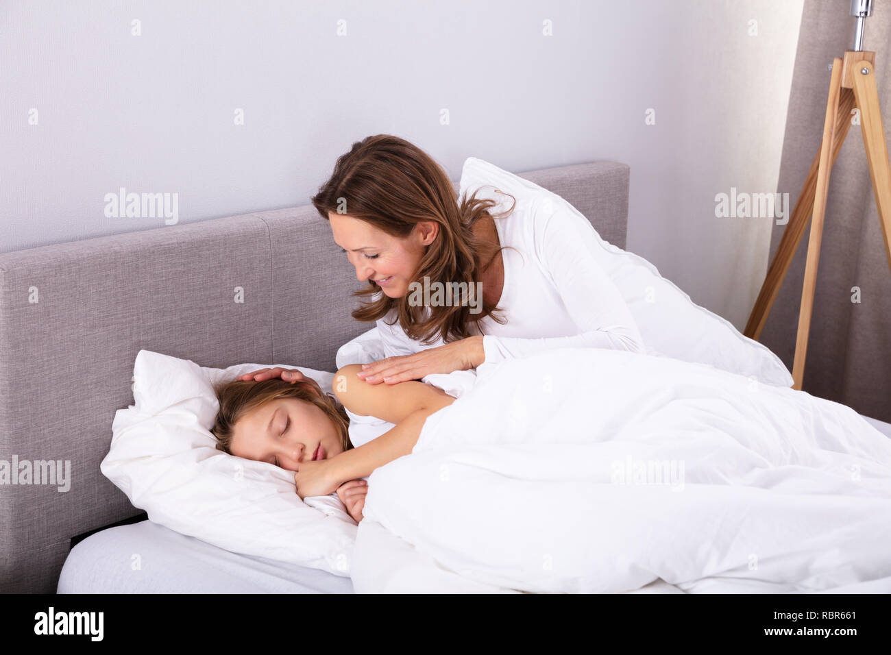 Reife Frau Aufwachen ihre Tochter schlief auf Bett im Schlafzimmer Stockfoto