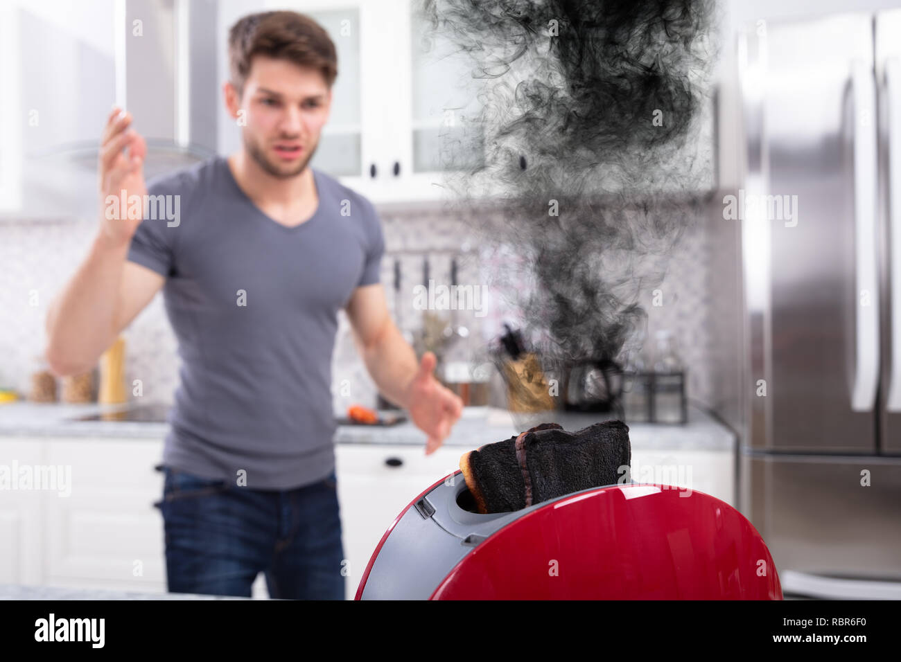 Frustriert junger Mann auf der Suche nach verbrannten Toast im Toaster in Küche Stockfoto